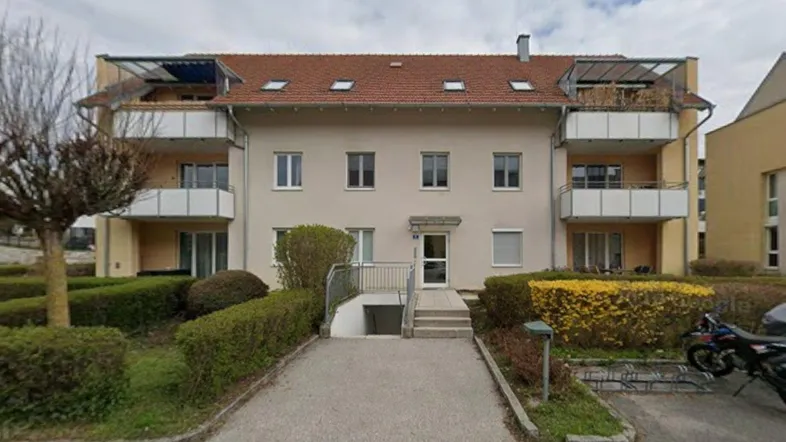 Mehrfamilienhaus mit mehreren Balkonen und einem Eingangsbereich mit Treppe zum Keller.