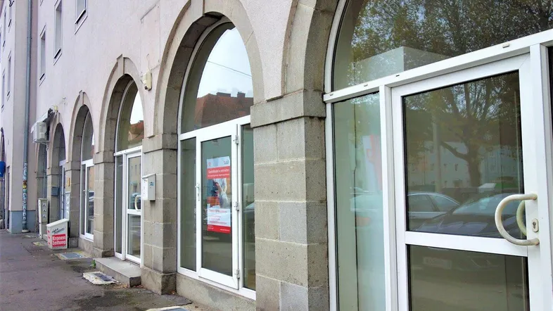 Gebäudefassade mit mehreren gewölbten Eingängen und großen Fenstern zur Straße hin.