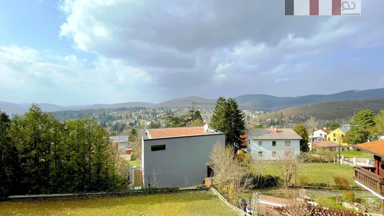 Weitläufiger Blick über die hügelige Landschaft mit Häusern und viel Grün unter bewölktem Himmel.