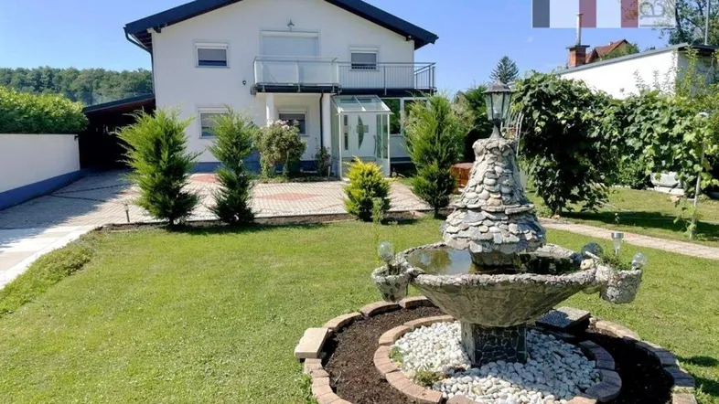 Gepflegter Vorgarten mit Zierbrunnen und dem Haupteingang des Einfamilienhauses unter blauem Himmel.