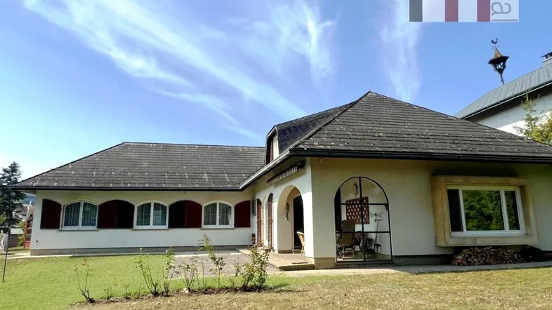 Traditionelles Haus mit Satteldach, Fensterläden und gepflegtem Vorgarten unter blauem Himmel.