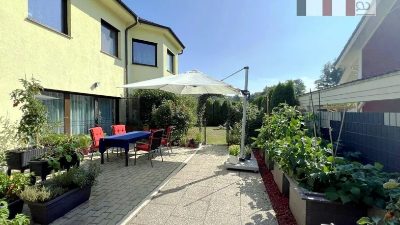 Große gepflasterte Terrasse mit Gartenmöbeln, Sonnenschirm und Hochbeeten, ideal für entspannte Stunden im Freien.