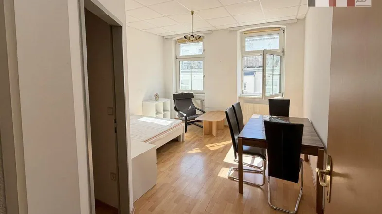 Heller Wohnraum mit Holzboden, Esstisch und Schlafbereich, ideal für ein Studio-Apartment.