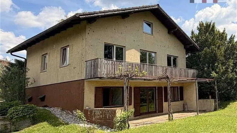 Freistehendes Haus mit Balkon und überdachter Terrasse, umgeben von viel Grün.