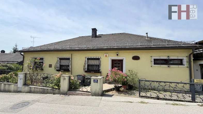 Gelbe Hausfassade mit schmiedeeisernen Fenstergittern und blühenden Pflanzen am Eingangsbereich.