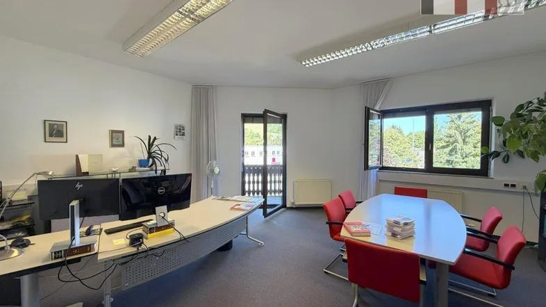 Geräumiges Büro mit mehreren Arbeitsplätzen, Konferenztisch und Zugang zu einem Balkon mit grüner Aussicht.