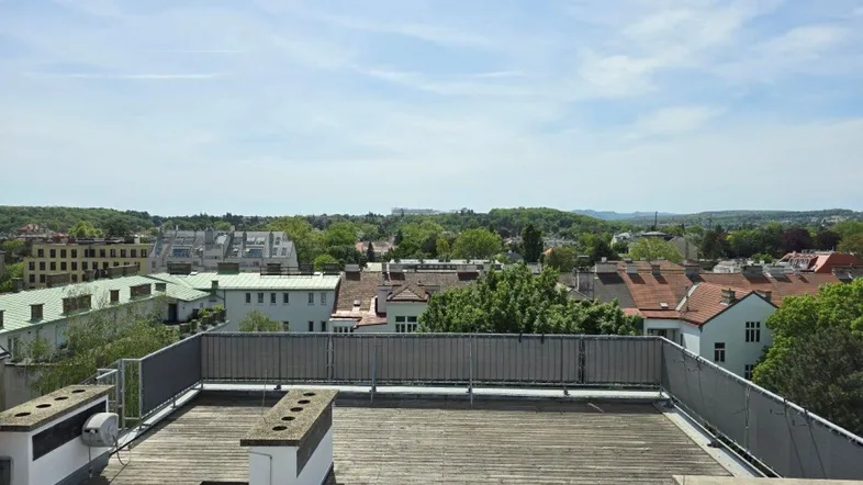 Große Dachterrasse mit Holzboden und weitem Blick über die Stadt und grüne Hügel.
