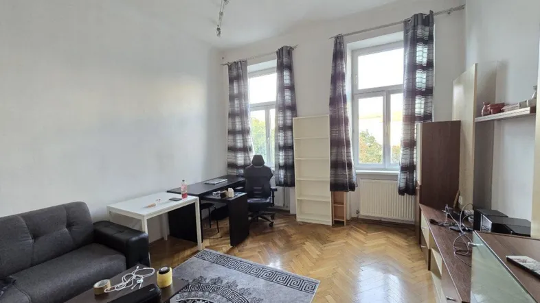 Helles Wohnzimmer mit Fischgrätparkett, einem Sofa, Schreibtisch und einem Teppich.
