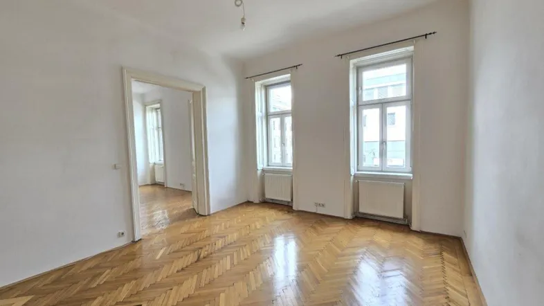 Helles Zimmer mit Fischgrätparkett und hohen Fenstern, das viel natürliches Licht hereinlässt.