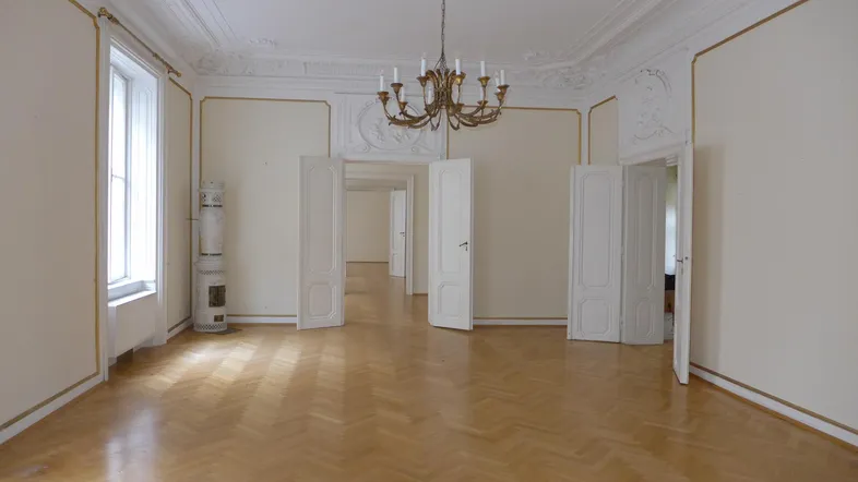 Helles Zimmer mit Fischgrätparkett, hohen Decken und Stuckverzierungen, ideal für Wohn- oder Essbereich.