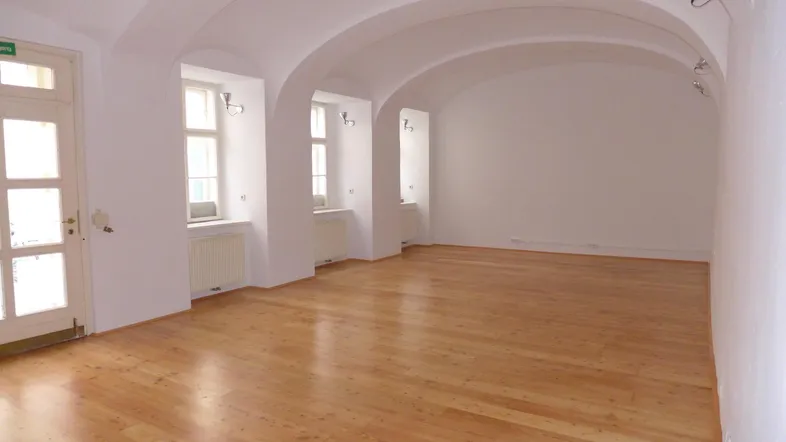 Heller, leerer Raum mit gewölbter Decke, Holzboden und mehreren Fenstern, ideal für Wohn- oder Bürozwecke.