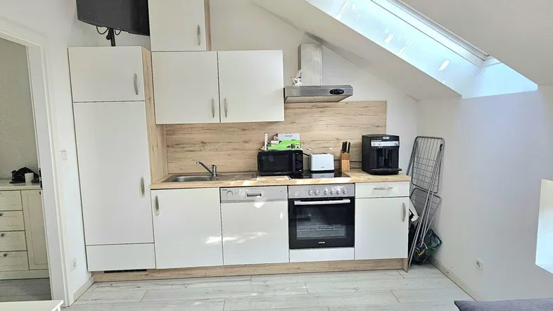 Moderne Küchenzeile in einer Dachgeschosswohnung mit Schrägdach, ausgestattet mit Geräten und einem Dachfenster.