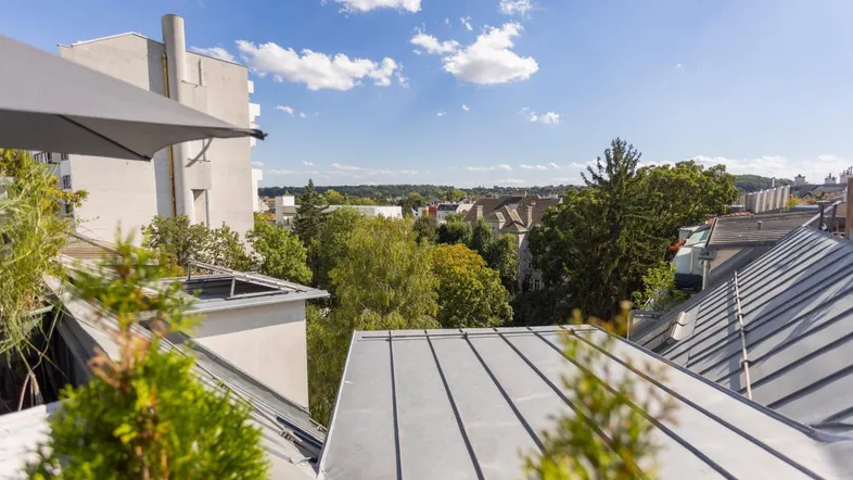 Blick über die Dächer der Stadt mit viel Grün und einem Sonnenschirm auf der Dachterrasse.