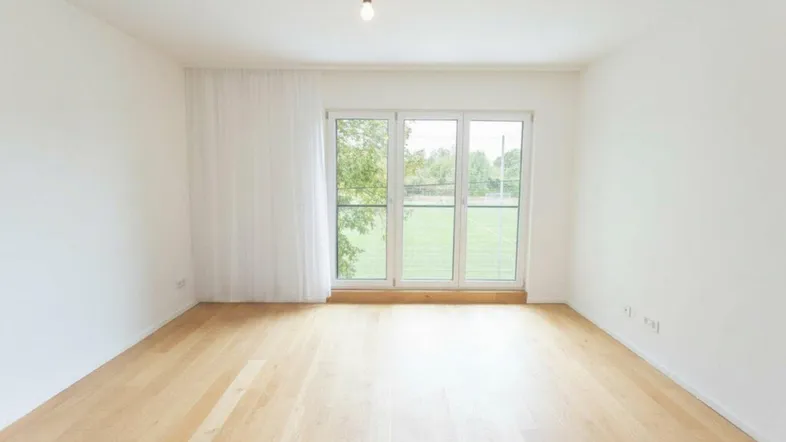 Helles Zimmer mit Parkettboden und großen Fenstern mit Blick ins Grüne.
