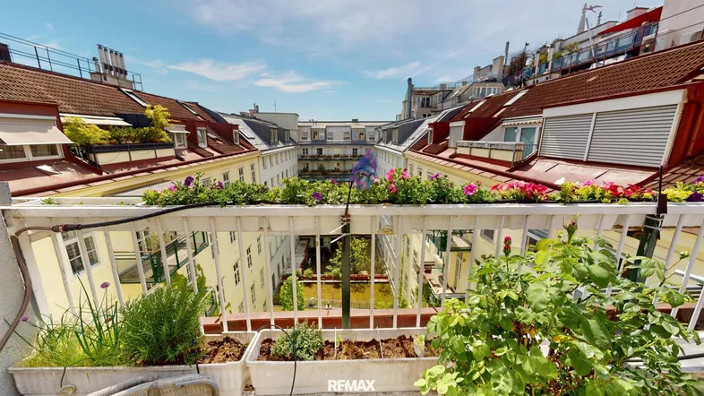 Blick vom Balkon auf den begrünten Innenhof mit Blumenkästen und umliegenden Gebäuden.
