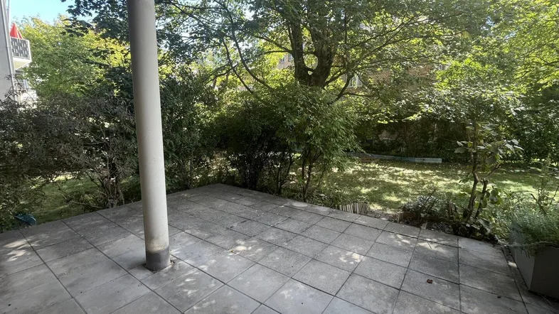 Geräumige Terrasse mit Steinplatten und Blick auf den grünen Gartenbereich.