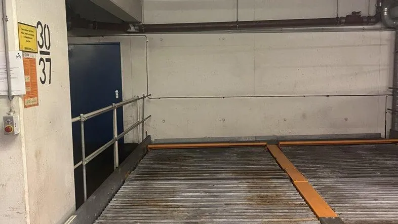 Tiefgaragenstellplatz mit einem mechanischen Parksystem für zwei Fahrzeuge und blauer Tür.
