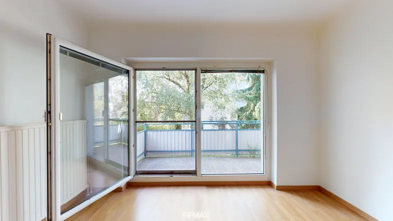 Helles Zimmer mit Holzboden und Zugang zu einem Balkon, ideal als Wohnbereich nutzbar.