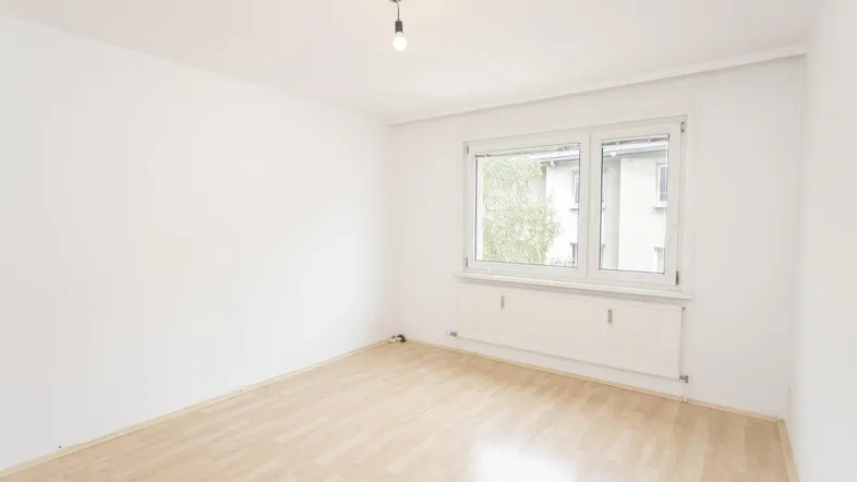Helles, leeres Zimmer mit Laminatboden und Fenster, bereit zur individuellen Gestaltung.