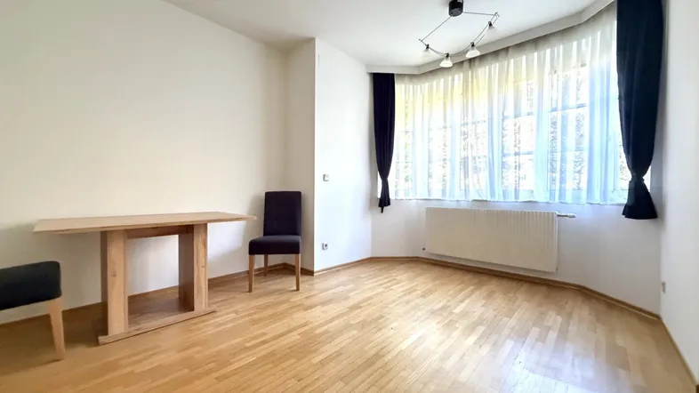Helles, leeres Zimmer mit Parkettboden und einem Erkerfenster, das viel Tageslicht hereinlässt.
