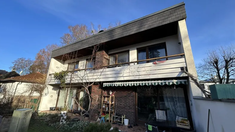 Mehrfamilienhaus mit Balkonen, Terrasse und Gartenbereich unter blauem Himmel.