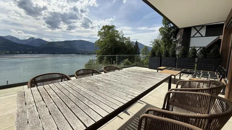 Große Terrasse mit Holztisch und Stühlen, bietet einen atemberaubenden Blick auf den See und die Berge.