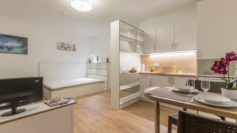 Helles Studio-Apartment mit integrierter Küchenzeile, Essbereich und Schlafbereich auf Laminatboden.