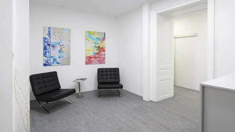 Heller Empfangsbereich mit zwei modernen schwarzen Sesseln und abstrakten Kunstwerken an der weißen Wand.