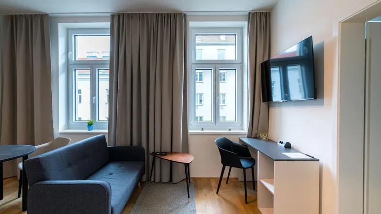 Heller Wohnbereich mit Sofa, Schreibtisch und Fernseher an der Wand.