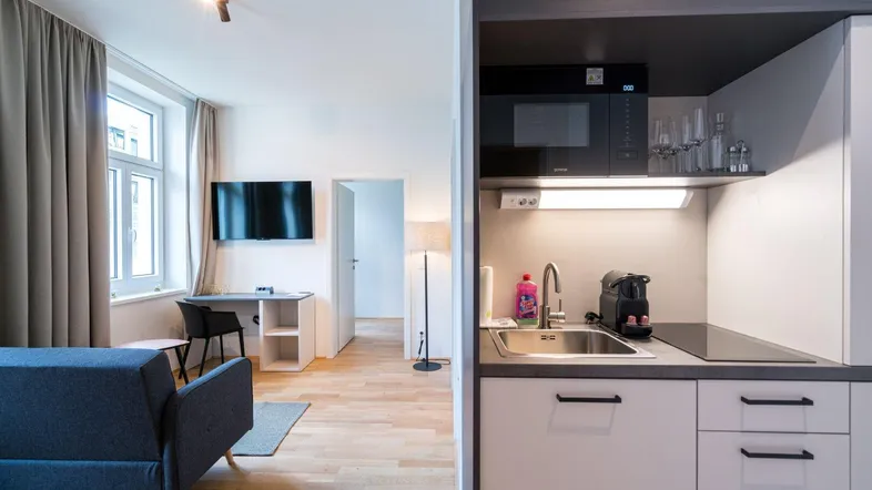 Moderner Wohnbereich mit integrierter Küchenzeile, Sofa und Arbeitsplatz, hell und funktional eingerichtet.