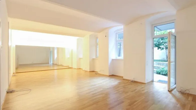 Großer, heller Raum mit Holzparkett, einer Spiegelwand und direktem Zugang zu einem kleinen Gartenbereich.