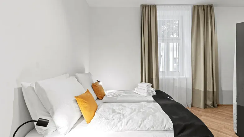 Helles Schlafzimmer mit Doppelbett, Nachttischlampe und Vorhängen am Fenster.
