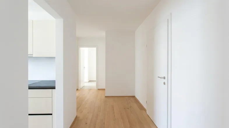 Heller Flur mit Holzparkettboden und Zugang zu angrenzenden Räumen, inklusive einem Blick in die Küche.