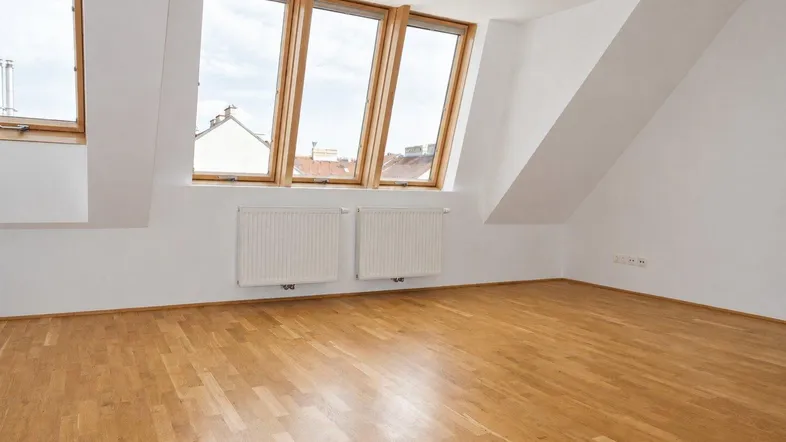 Heller, leerer Raum mit Dachschrägen, Dachfenstern und Parkettboden, ideal als Wohnzimmer.