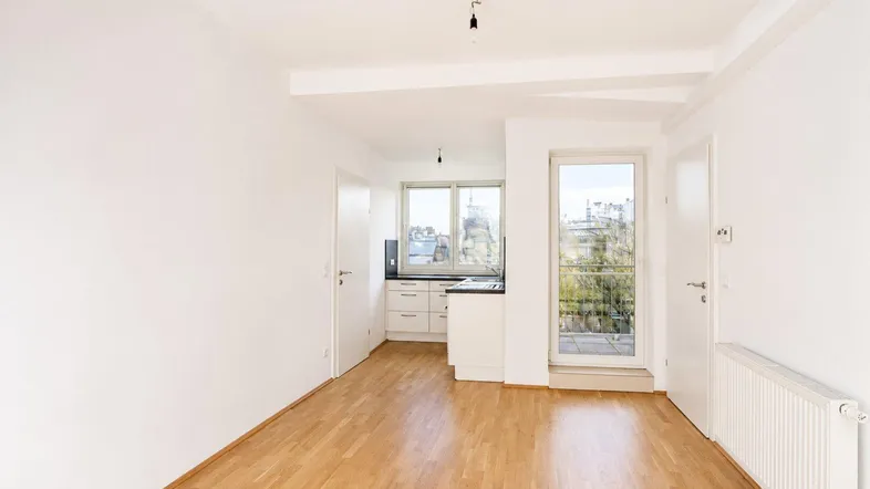Heller offener Wohnbereich mit integrierter Küche, Parkettboden und Zugang zum Balkon.