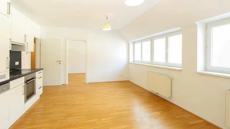 Heller offener Wohnbereich mit integrierter Küche, Parkettboden und großen Fenstern.