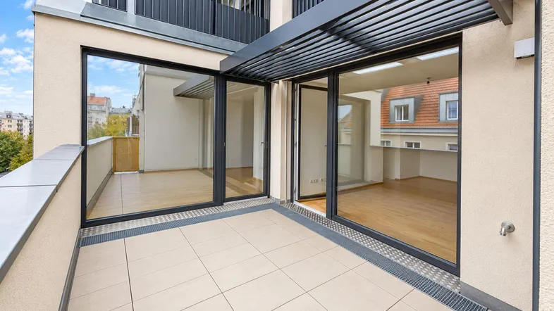 Geräumiger Balkon mit Fliesenboden und Blick auf die Stadt, verbunden mit dem Innenbereich durch große Glasfronten.
