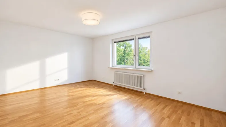 Heller, leerer Raum mit Parkettboden und großem Fenster, ideal als Wohn- oder Schlafzimmer.