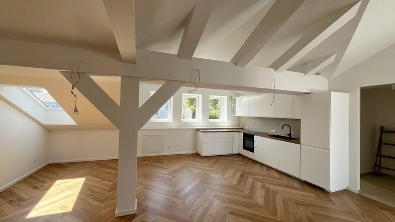 Heller offener Wohnbereich mit moderner Einbauküche, Fischgrätparkett und sichtbaren Dachbalken.