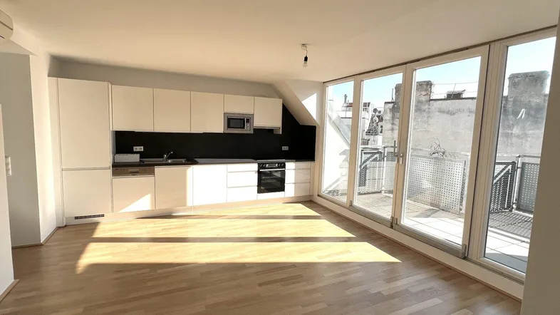Heller offener Wohn-Essbereich mit moderner Einbauküche, Holzboden und Zugang zu einer sonnigen Terrasse.