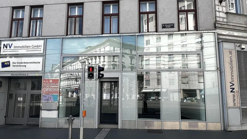 Außenansicht eines Geschäftsgebäudes mit großer Glasfassade und Schaufenstern im Erdgeschoss.