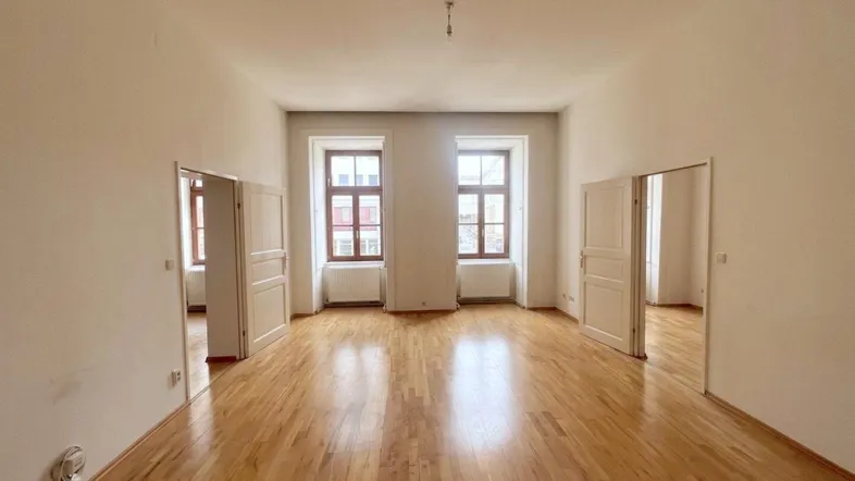 Helles, leeres Zimmer mit Parkettboden und zwei Fenstern, bereit zur individuellen Gestaltung.