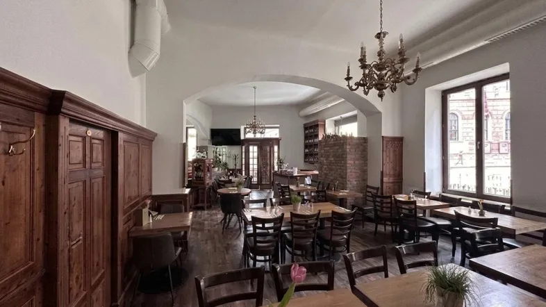 Geräumiger Restaurantbereich mit Holztischen, traditionellem Kronleuchter und großen Fenstern, die viel Tageslicht hereinlassen.