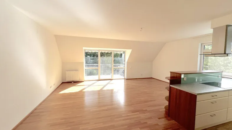 Heller offener Wohnbereich mit Holzboden, Dachschrägen und Zugang zum Balkon.