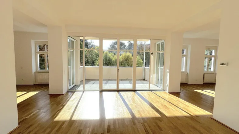 Helles Wohnzimmer mit Parkettboden, großen Fenstern und direktem Zugang zu einem Balkon.