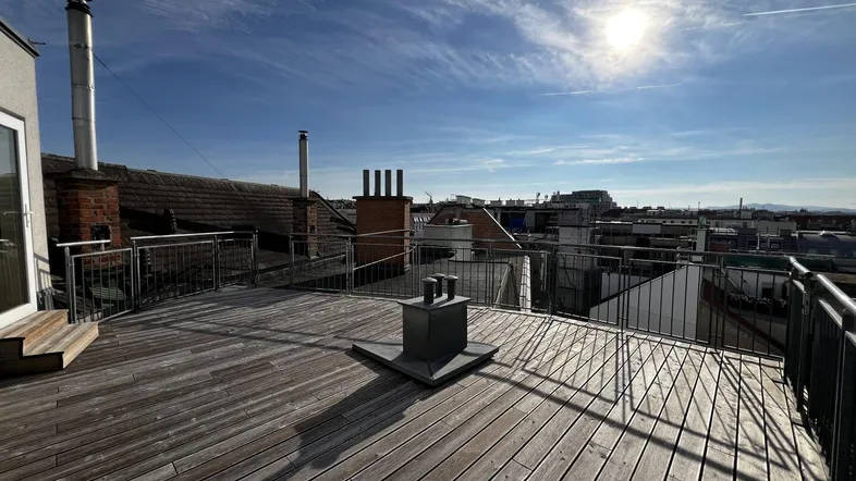 Geräumige Dachterrasse mit Holzboden und weitem Blick über die Stadt unter blauem Himmel.