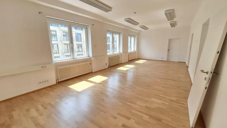 Geräumiger, leerer Büroraum mit hellem Parkettboden und großen Fenstern, die viel Tageslicht hereinlassen.