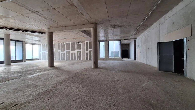 Großer, unfertiger Innenraum mit Betonboden und -decken, Säulen und großen Fenstern, bereit für den Ausbau.