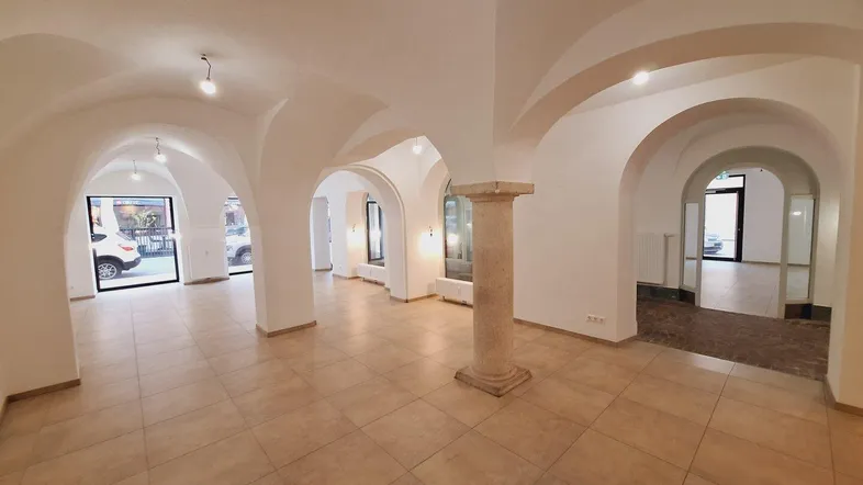 Geräumiger Gewerberaum mit hohen Gewölbedecken, Fliesenboden und einer markanten Steinsäule in der Mitte.