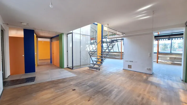 Geräumiger offener Wohnbereich mit Holzboden, bunten Akzentwänden und einer modernen Metalltreppe.